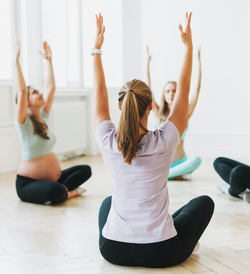 Pregnant women raising their arms together in a prenatal yoga class