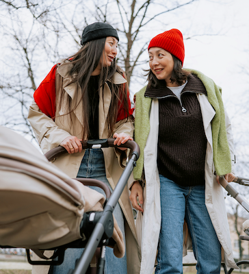 Two mothers smiling at each other while walking outside with a stroller