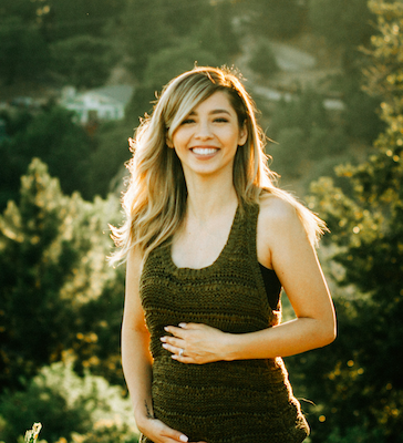 Smiling pregnant woman in a dark tank top standing outdoors at golden hour